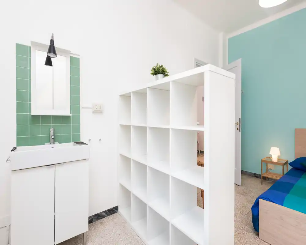 Bright, modern bedroom corner with a visible single/double bed, bedside table with lamp and a white cubed room divider; fresh mint accent wall and clean minimalist styling.