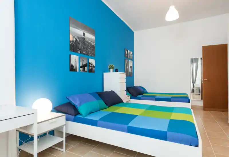 Chambre lumineuse avec deux lits simples disposés dans un cadre moderne, mur d'accent bleu vif, tables de chevet et affiches décoratives épurées.
