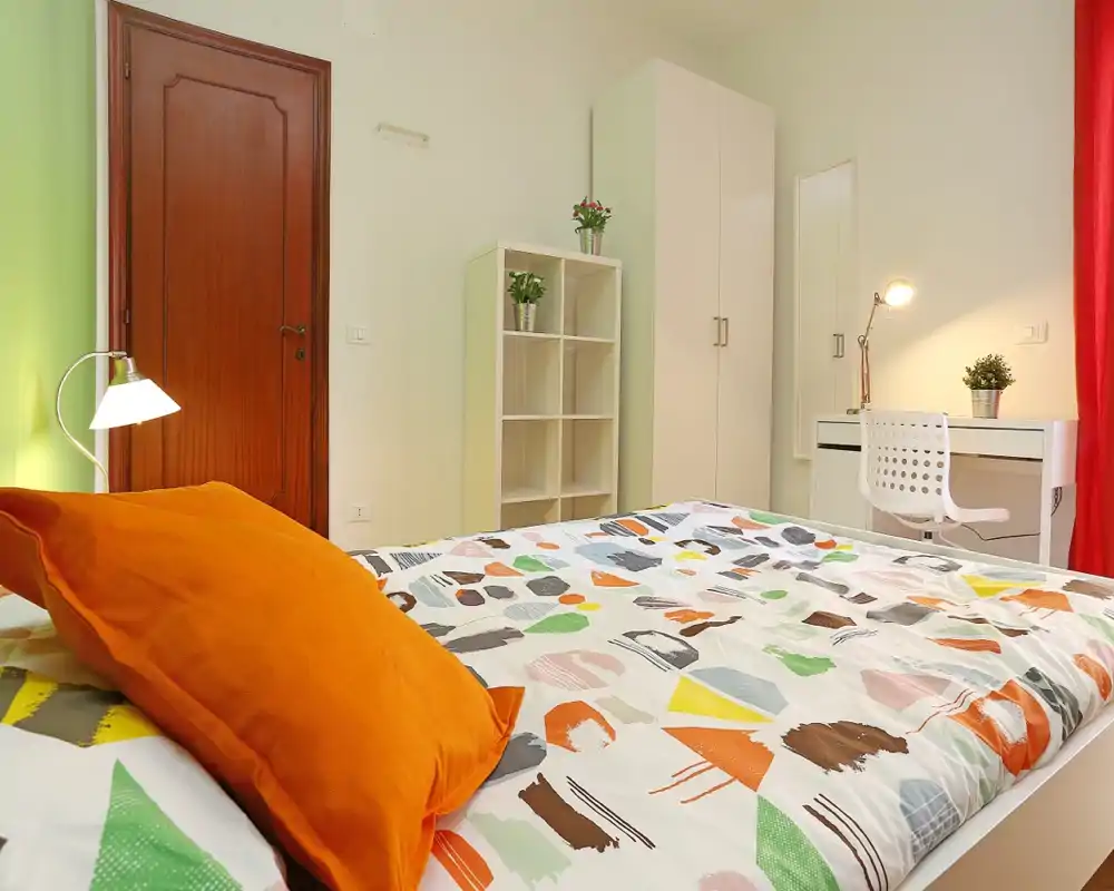 Dormitorio luminoso y bien presentado con ropa de cama colorida, armario, escritorio y lámpara de noche — acogedor y perfecto para fotos del anuncio.