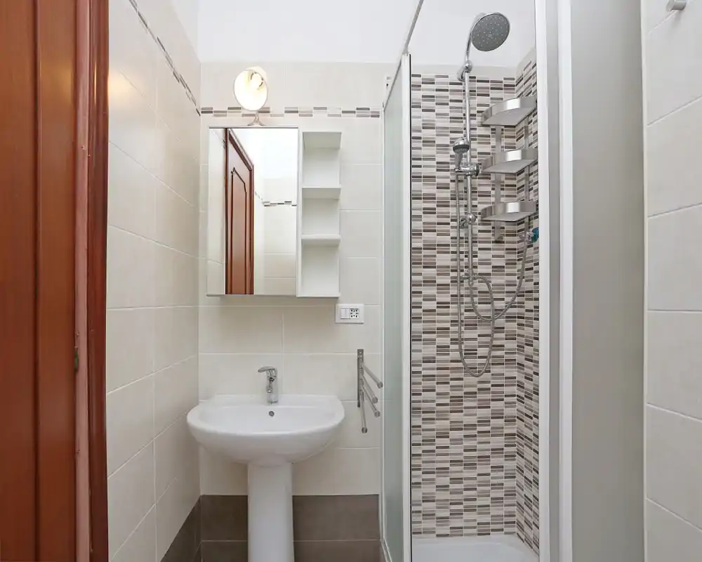Baño compacto y moderno con lavabo de pie, armario con espejo y ducha alicatada con mampara de cristal y columna de ducha tipo lluvia.