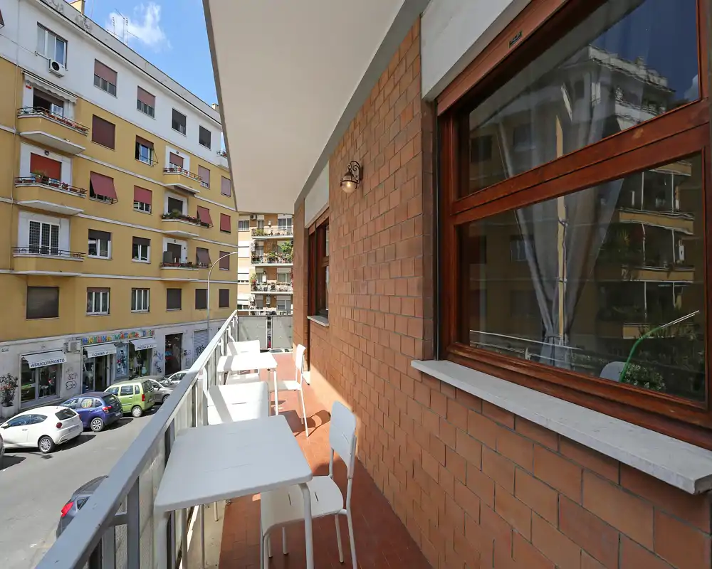 Balcón urbano soleado con mesas y sillas pequeñas, suelo de terracota y vista a la calle — ideal para el café de la mañana.