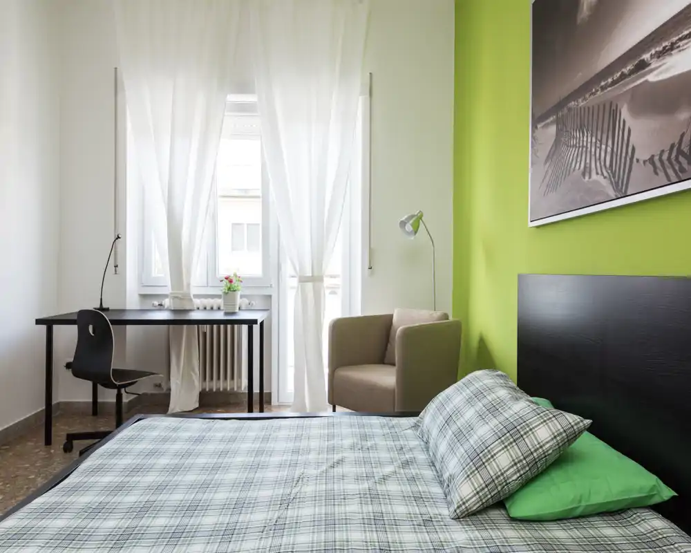 Bright, modern bedroom with a comfortable double bed, green accent wall and a desk by the window—ideal for work and rest.