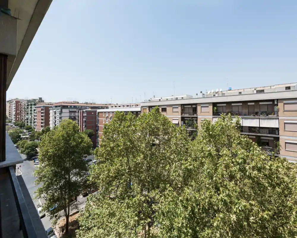 Vista dal balcone soleggiata su viali alberati e palazzi vicini — panorama urbano luminoso e aperto, ideale per mostrare gli aspetti esterni dell’immobile.