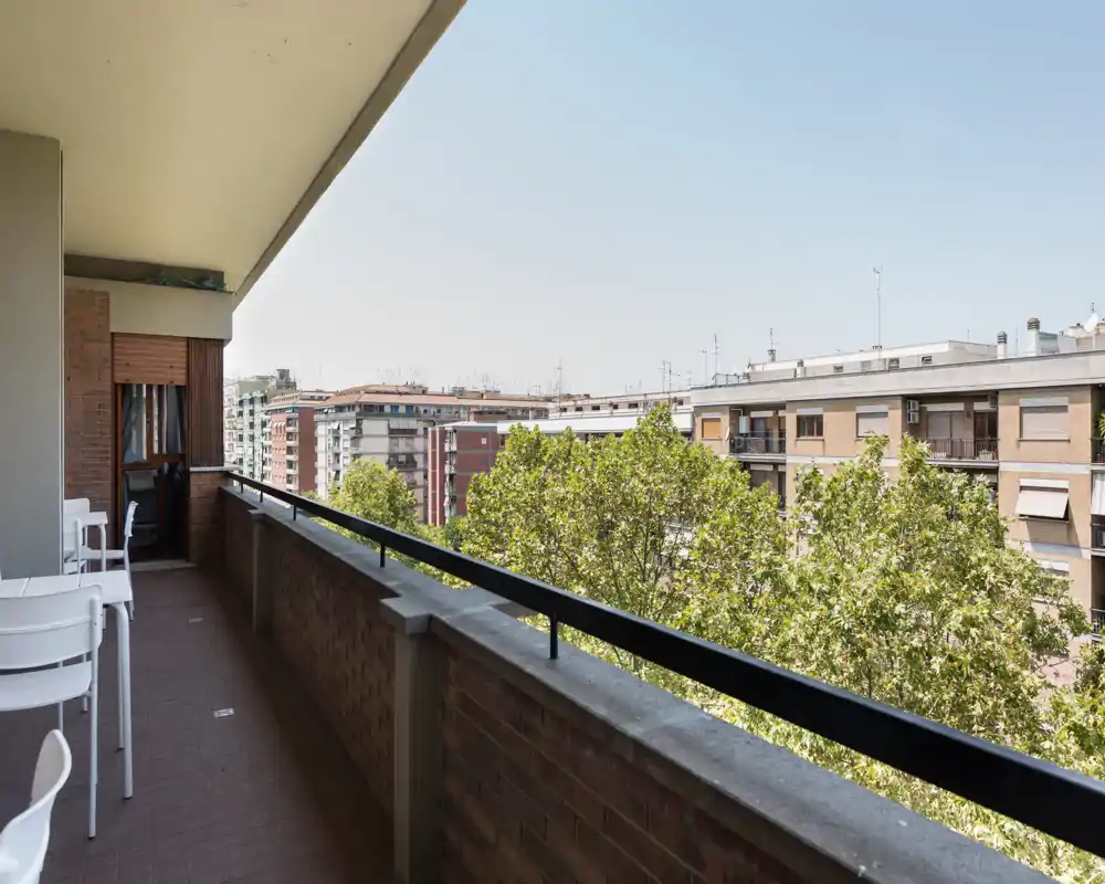 Balcone soleggiato con posti a sedere e ampia vista su edifici e alberi della città; ideale per colazione o relax all'aperto.