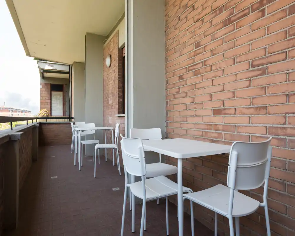 Balcone soleggiato con parete in mattoni e tavolo e sedie bianche da esterno, ideale per pranzi informali o relax all'aperto.
