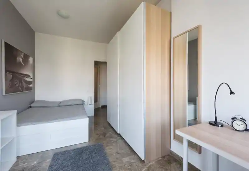 Camera da letto minimalista con letto matrimoniale, armadio integrato, scrivania e specchio a figura intera; toni neutri e pavimento in marmo per un aspetto pulito e moderno.