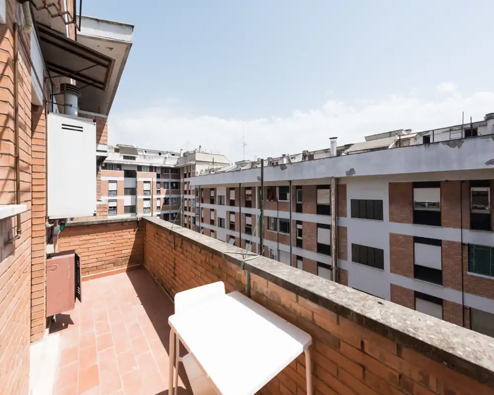 Piccolo terrazzo soleggiato con pavimento in cotto, muretto in mattoni e un tavolino — ideale per colazione all'aperto e vista sulla città.