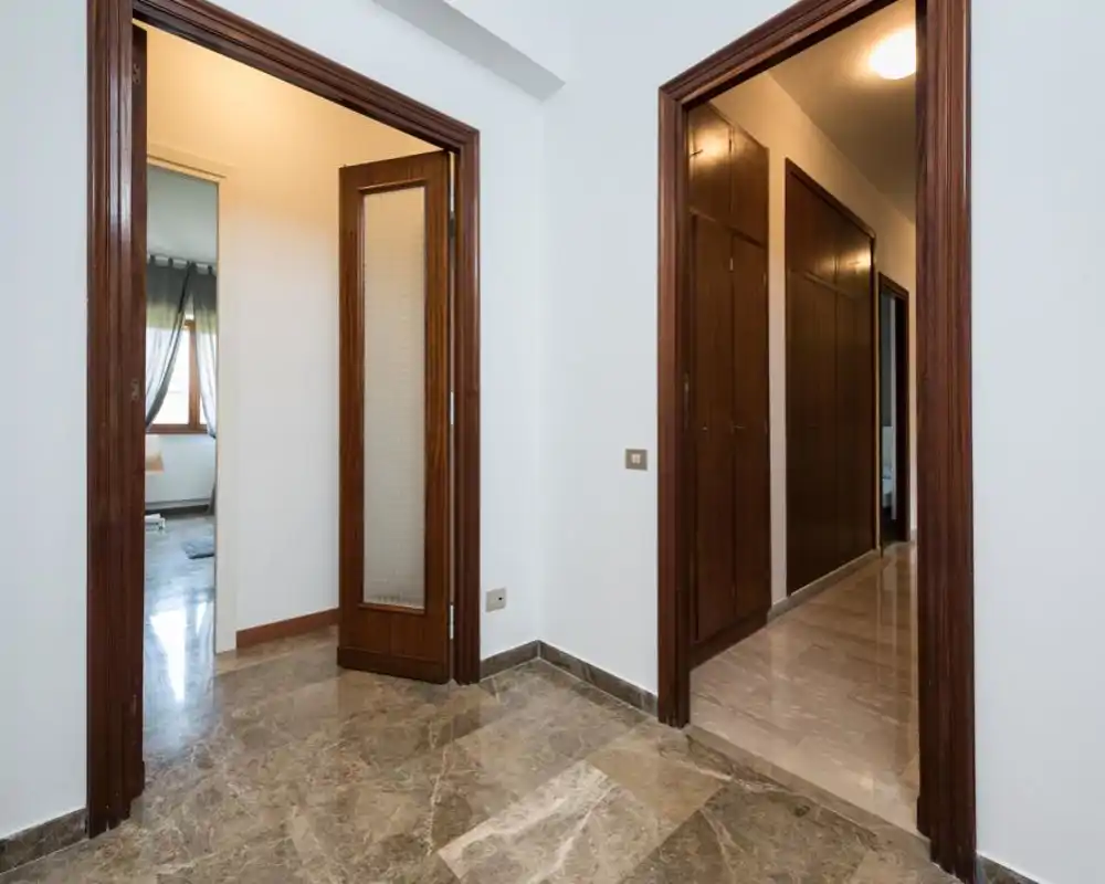 Ingresso/corridoio luminoso e pulito con pavimento in marmo lucido e cornici delle porte in legno che conducono alle stanze adiacenti.