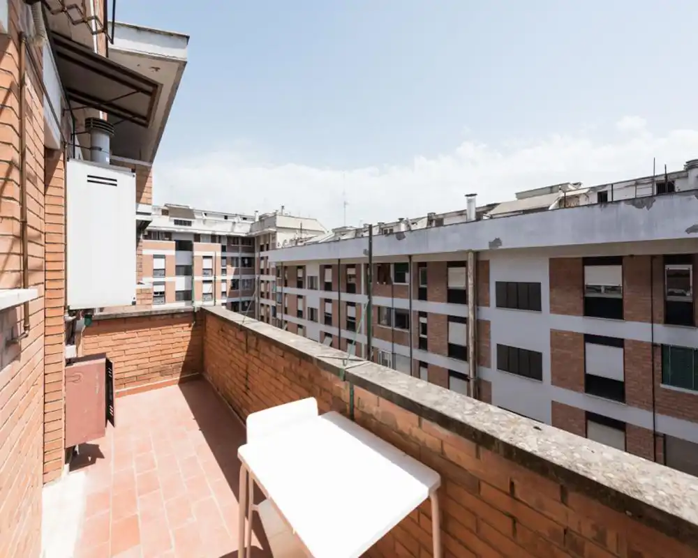 Balcone privato soleggiato con pavimento in cotto, parapetto in mattoni e un piccolo tavolo bianco — ideale per colazione con vista sulla città.