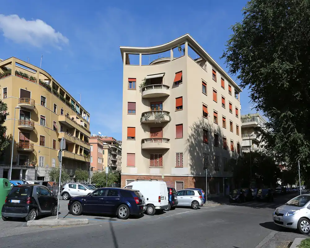 Vista de la calle con un edificio residencial, coches aparcados y cielo azul, ideal para mostrar el exterior y el vecindario.