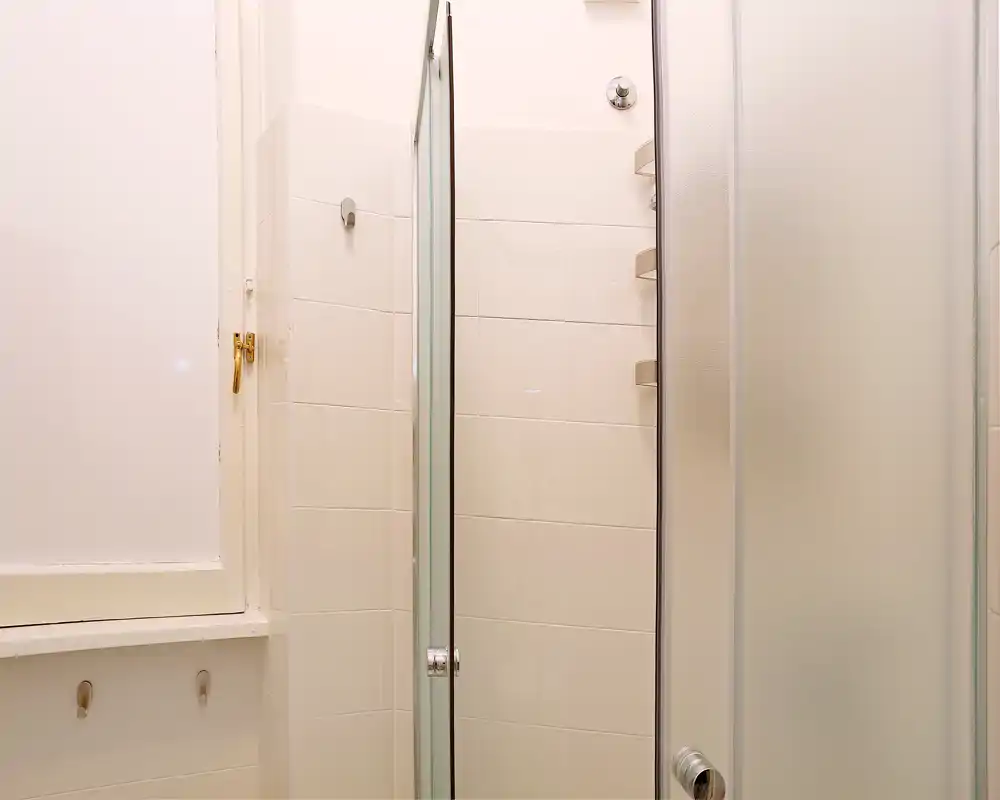 Baño compacto con ducha de vidrio, paredes azulejadas blancas y puerta corredera esmerilada — diseño limpio y funcional, ideal para un anuncio.