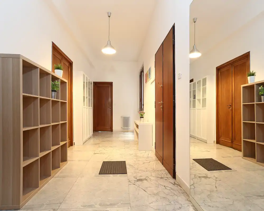 Entrada luminosa con suelos de mármol, puertas de madera y estanterías prácticas; un gran espejo amplía la sensación de espacio.