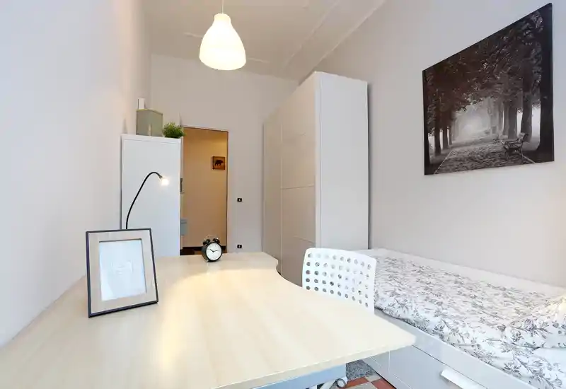 Bright, tidy single bedroom with a work desk, bedside storage and framed wall art. The space is well-lit and neatly staged for a comfortable stay.