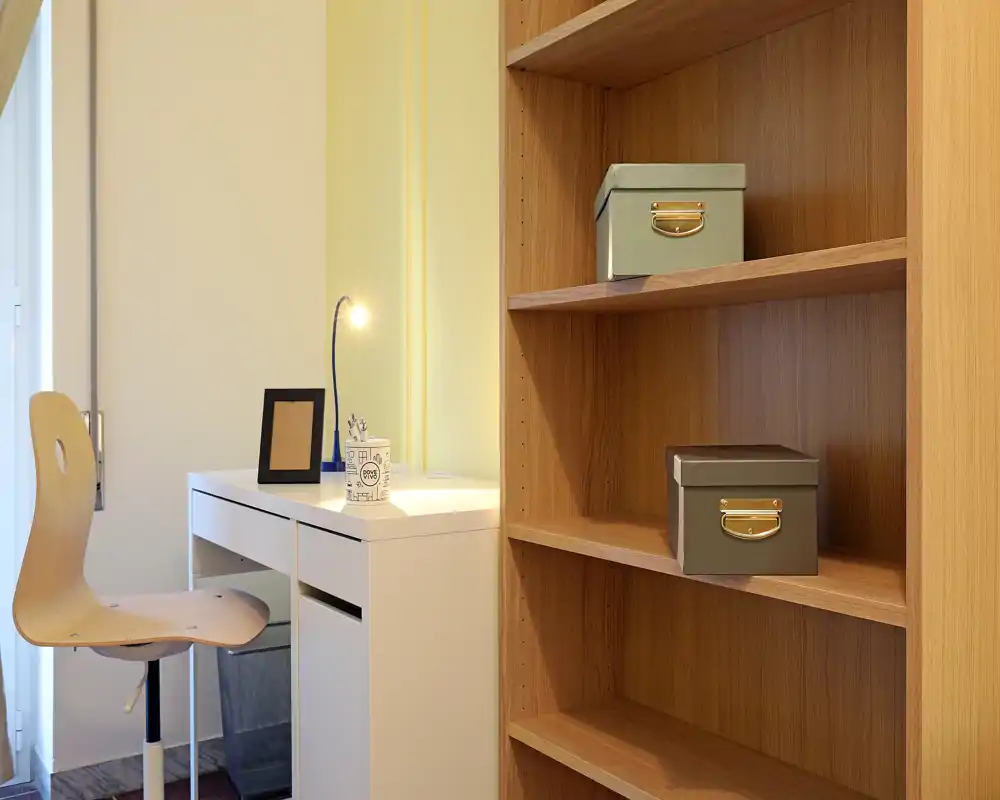 Rincón de estudio luminoso y minimalista con escritorio blanco, silla de madera y estantería abierta — un espacio de trabajo ordenado ideal para alquileres temporales.
