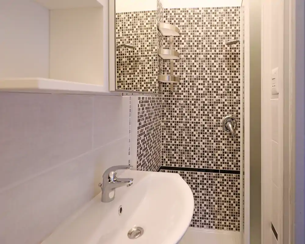 Bagno moderno compatto con lavabo bianco e doccia piastrellata con mosaico bianco e nero e rubinetteria in acciaio.