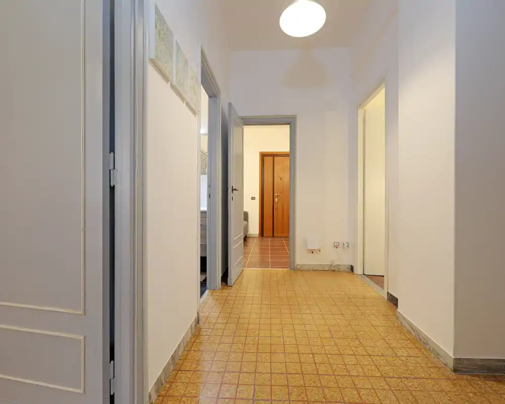 Ingresso/corridoio luminoso e ben inquadrato con pavimento piastrellato a motivi e più porte che conducono alle stanze adiacenti. Pareti bianche neutre e illuminazione a soffitto rendono l'ambiente pulito e funzionale.