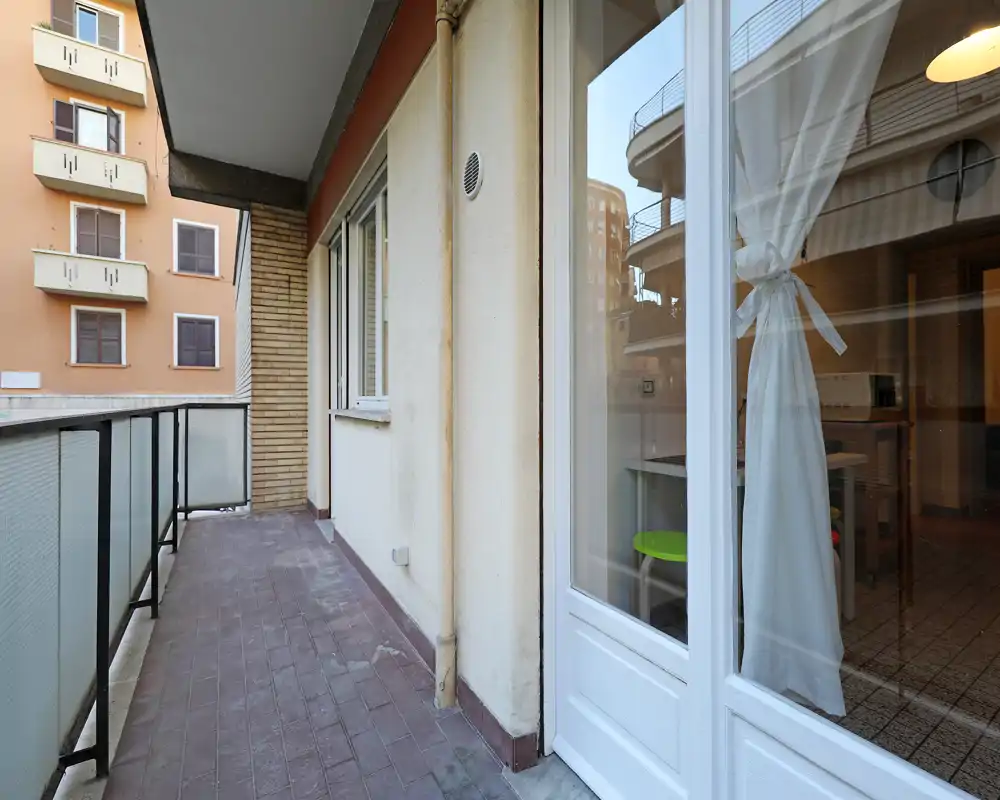 Balcone stretto con pavimento piastrellato, ringhiera metallica e accesso all'appartamento tramite porta a vetri — adatto per piccoli posti a sedere o piante.