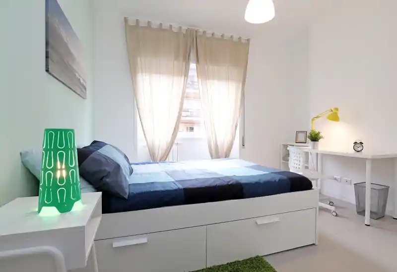 Bright, neatly staged bedroom with a double bed, coordinating bedding and a small desk by the window; soft natural light and modern minimal decor create a calm, inviting space.
