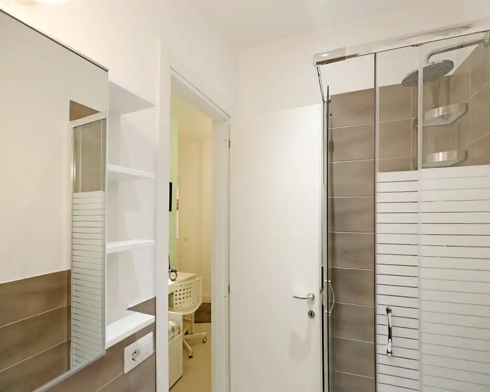 Salle de bains moderne avec douche vitrée, carrelage aux tons neutres et armoire miroir ; espace lumineux, propre et bien entretenu.