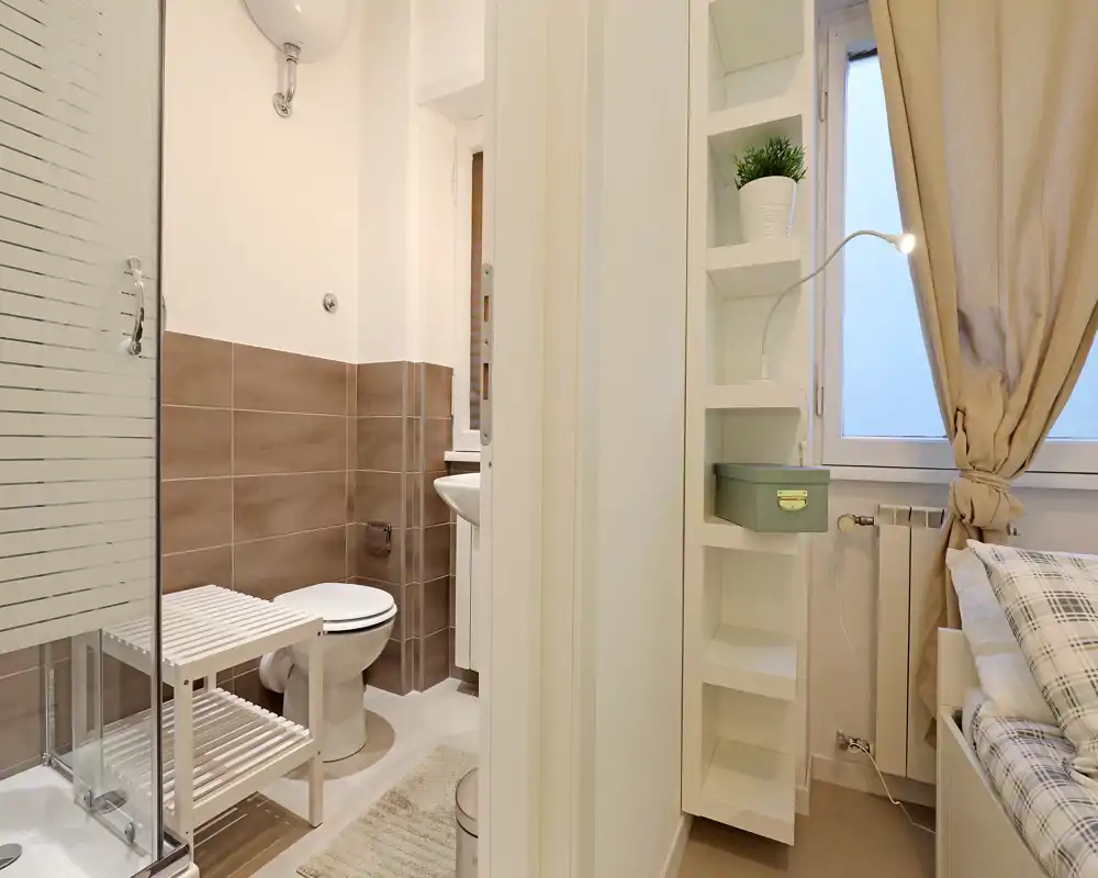 Salle de bain compacte avec cabine de douche, WC et lavabo ; carrelage neutre et petite étagère de rangement. Lumineuse, propre et fonctionnelle, adaptée à un petit appartement.