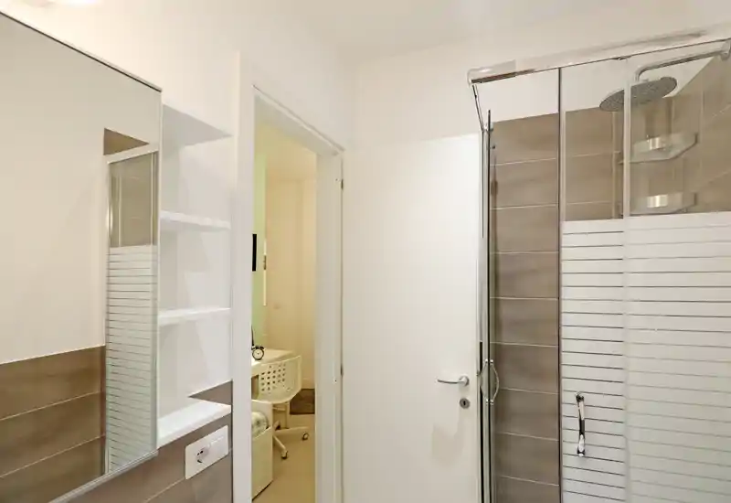 Salle de bains moderne avec douche vitrée, carrelage aux tons neutres et armoire miroir ; espace lumineux, propre et bien entretenu.