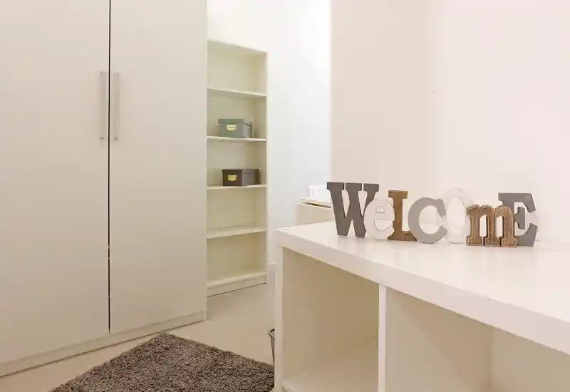 Espace de vie minimal et lumineux avec rangements intégrés, une déco "Welcome" et un tapis moelleux, parfait pour un coin entrée/salon soigné.