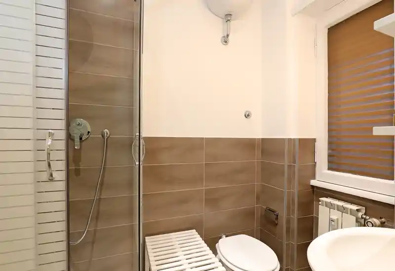 Salle de bains compacte et moderne avec cabine de douche en verre, équipements muraux et carreaux bruns neutres — lumineuse et propre.