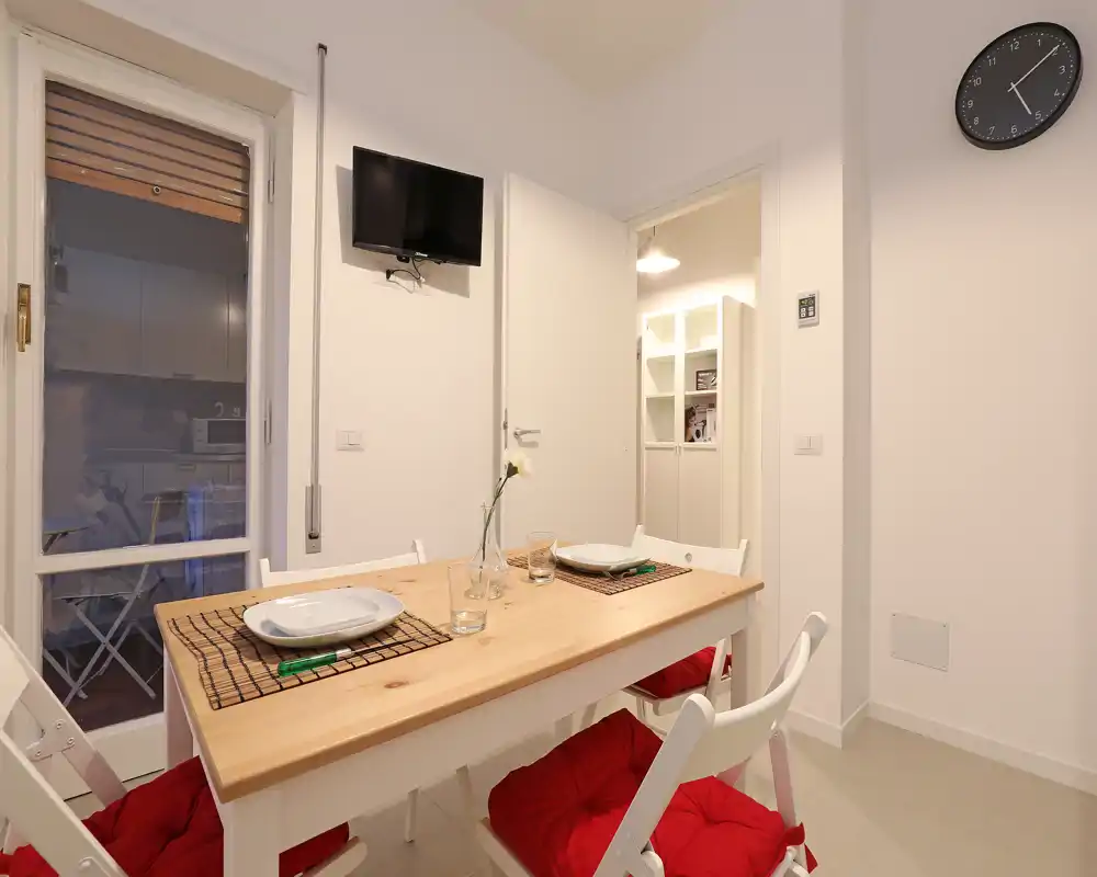 Bright, modern dining area with a wooden table set for two, red chair cushions and minimal decorative touches—ideal for compact apartment listings.
