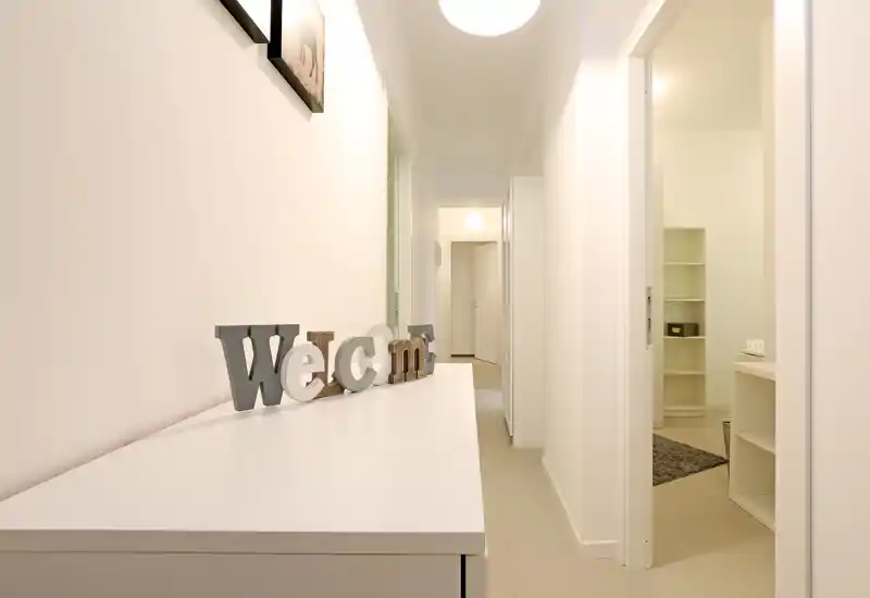 Couloir lumineux et minimaliste avec une console et des lettres décoratives « Welcome » ; tons neutres et portes menant aux pièces adjacentes.