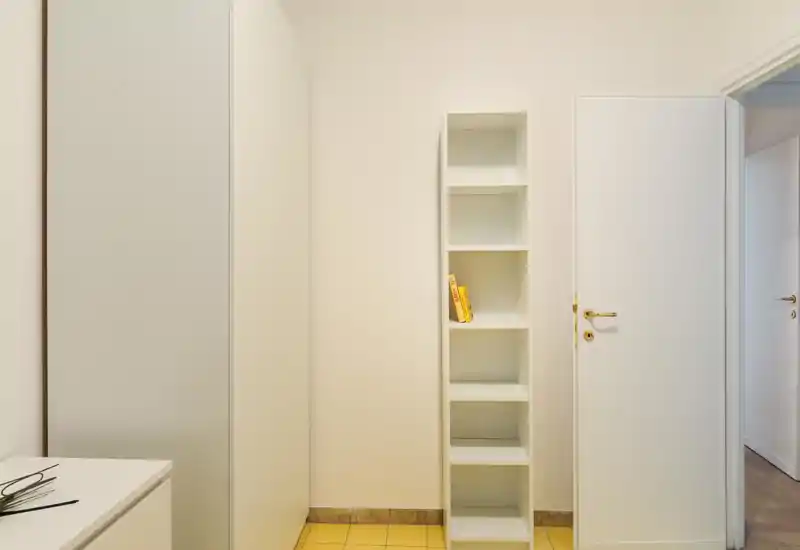 Piccolo ingresso/anticamera luminoso con scaffalatura a incasso e porta bianca — ambiente minimal e ordinato ideale per riporre cappotti o oggetti.