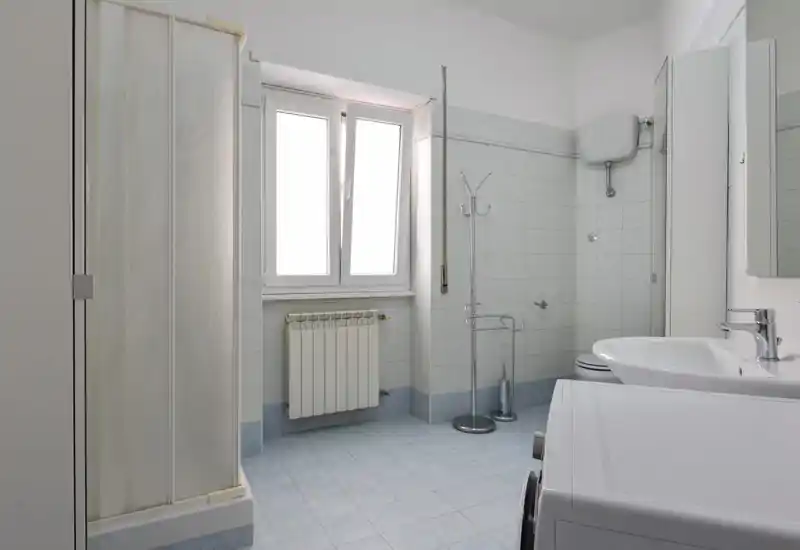 Bagno pulito e luminoso con piastrelle, lavabo e box doccia visibile; la luce naturale dalla finestra rende l'ambiente arioso.