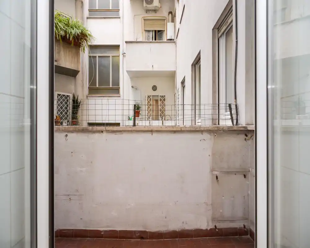 Piccolo balcone interno con pavimento piastrellato e muretto basso che dà su facciate adiacenti; adatto per una piccola zona relax esterna o piante.