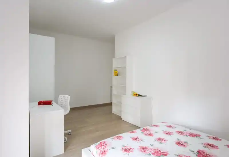 Dormitorio luminoso y minimalista con colcha floral, mobiliario blanco y un pequeño escritorio; estilo limpio y moderno, ideal para anuncios.
