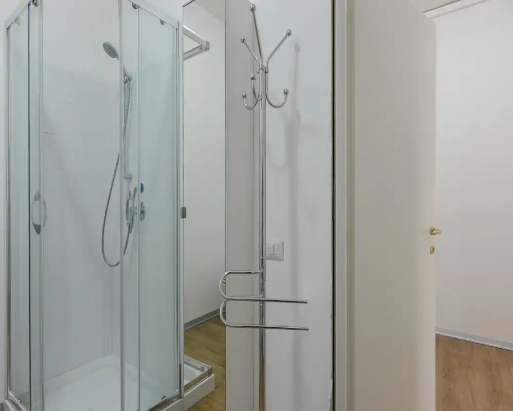 Baño compacto y moderno con plato de ducha y mampara de vidrio, cabezal de ducha cromado y azulejos blancos. Limpio, luminoso y de diseño minimalista, ideal para anuncios de alquiler.