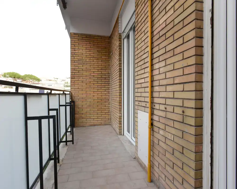 Balcón soleado y estrecho con suelo de baldosas, muros de ladrillo y barandilla de cristal esmerilado — perfecto para una pequeña zona exterior o plantas.