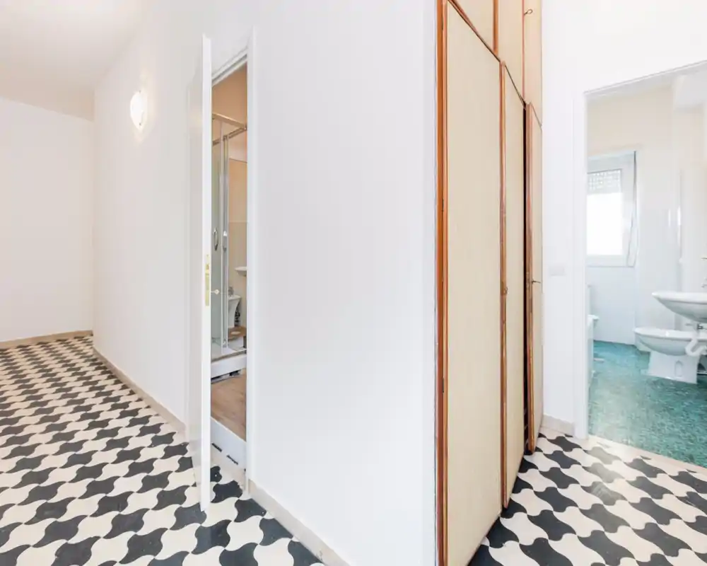 Corridoio/ingresso luminoso con pavimento a piastrelle a motivo, armadi a muro e porte che conducono ai bagni. Pareti bianche pulite e layout semplice e funzionale, adatto come ingresso.