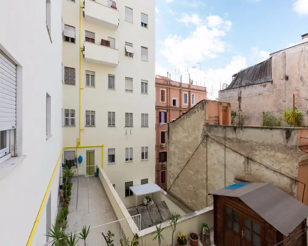 Terrazza interna soleggiata con vasi, pavimento piastrellato e vista sugli edifici: spazio esterno luminoso e riservato.