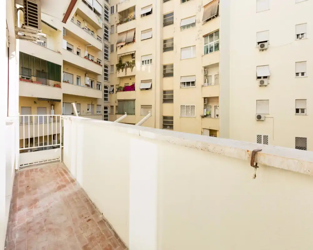 Balcone soleggiato e stretto con pavimento in piastrelle e parapetto solido, affaccia sulle facciate dei palazzi vicini — ideale per una piccola area relax o piante.