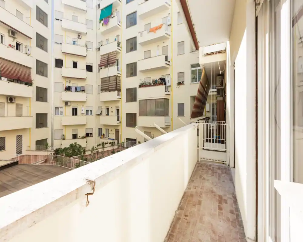 Balcone privato soleggiato con vista sul cortile interno, pavimento in piastrelle e ringhiera — ideale per caffè mattutino o stendere il bucato.
