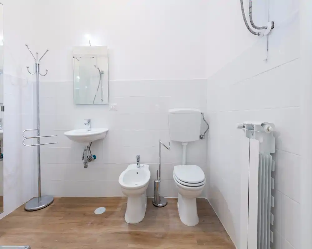 Bright, compact bathroom with white tiles, a sink, bidet and toilet shown in a clean modern layout.