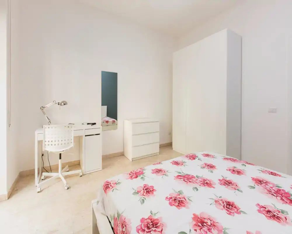 Camera da letto luminosa e minimal con copripiumino floreale, armadio bianco e piccolo angolo scrivania — arredo pulito e arioso ideale per un annuncio.