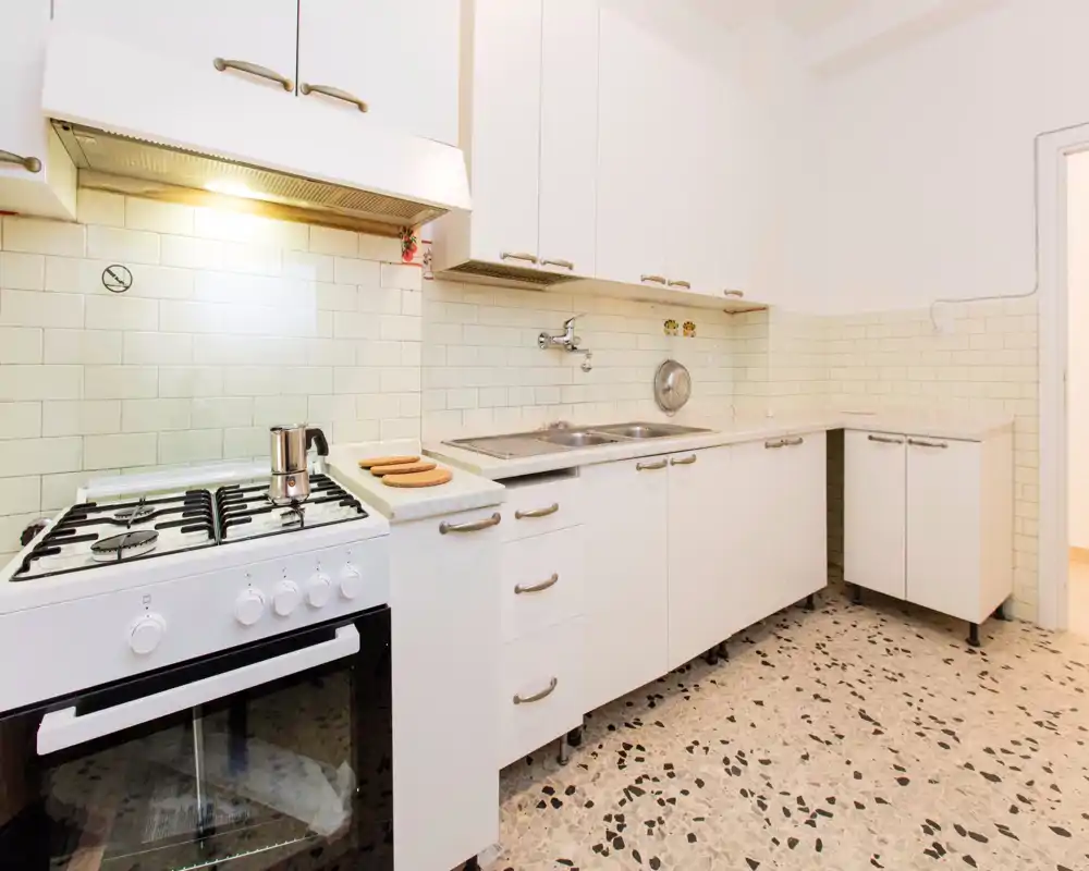 Cucina compatta e luminosa con mobili bianchi, fornello a gas e doppio lavello — layout pulito e funzionale, ideale per un appartamento piccolo.
