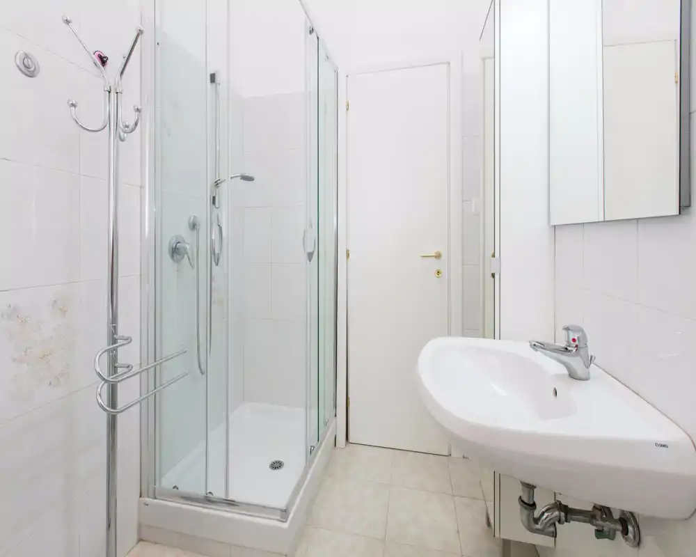 Bagno compatto e luminoso con box doccia in vetro, lavabo a parete e specchiera; ambiente pulito e dallo stile semplice.