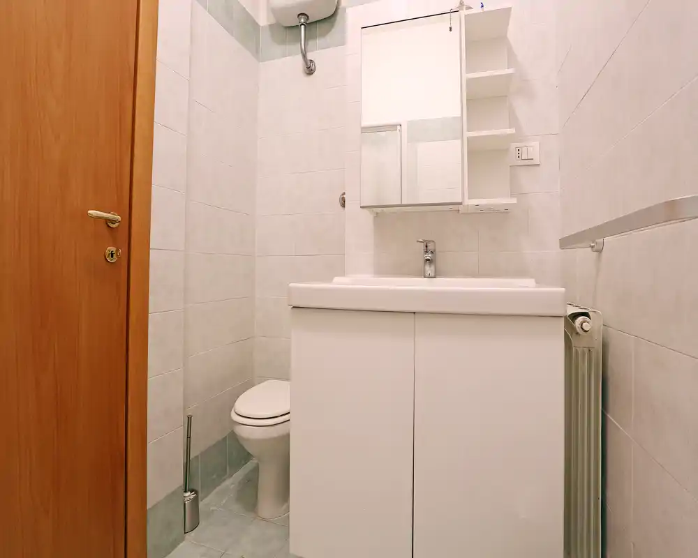 Baño pequeño y bien iluminado con lavabo con mueble, espejo-armario, inodoro y paredes alicatadas en tonos neutros. Distribución limpia y compacta, adecuada para un anuncio de alquiler.