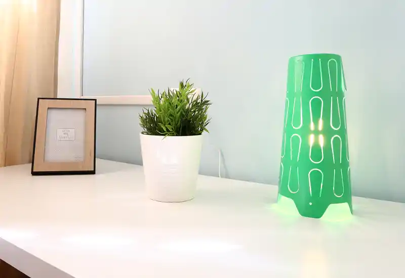 Piccolo angolo d'ingresso con vaso decorativo, cornice portafoto e una lampada verde moderna su una superficie bianca pulita.