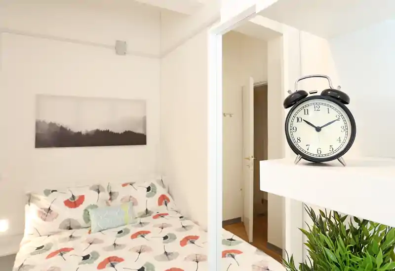 Camera da letto luminosa e accogliente con letto matrimoniale con copriletto decorato, cuscini e un quadro minimalista — perfetta per un soggiorno confortevole.