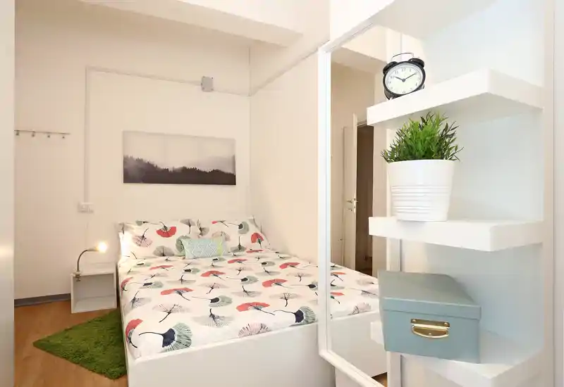 Camera da letto luminosa e compatta con letto matrimoniale con fantasia, lampada da comodino e dettagli decorativi che creano un ambiente accogliente.