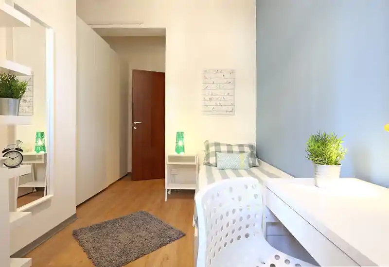 Habitación individual moderna y luminosa con cama hecha, escritorio y planta decorativa — ideal para estudiante o inquilino soltero.