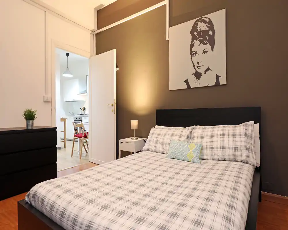 Camera da letto spaziosa e ben illuminata con letto matrimoniale, tessili accoglienti e quadro moderno; toni neutri e luce calda per un ambiente invitante.
