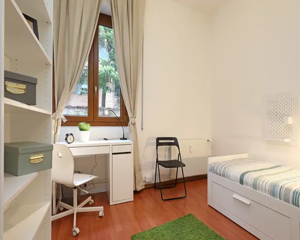 Camera da letto luminosa e minimal con letto singolo, scrivania vicino alla finestra e ripostigli ordinati; ideale per studente o ospiti.